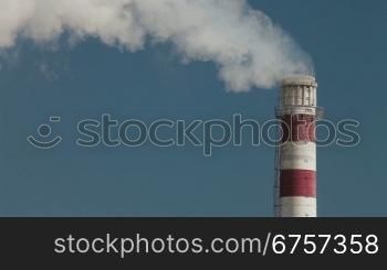 Industrial smokestack with billowing white smoke being pumped into the atmosphere against a blue sky
