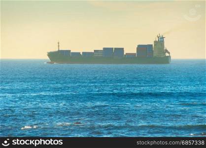 Industrial tanker full of containers in the ocean at sunset