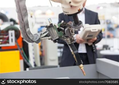 Industrial welding robot arm in the focus, blurred operator in the background