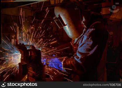 Industrial Worker at the car factory is welding assembly automotive part, closeup