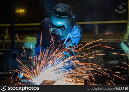 Industrial worker is welding automotive part in factory