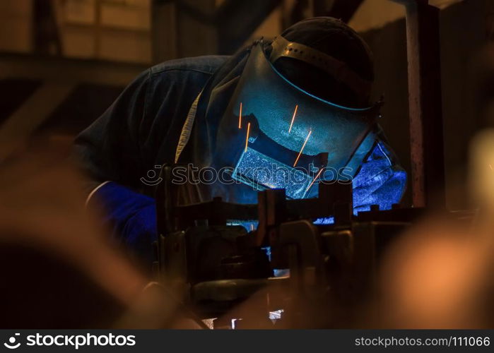 Industrial worker is welding metal part in factory