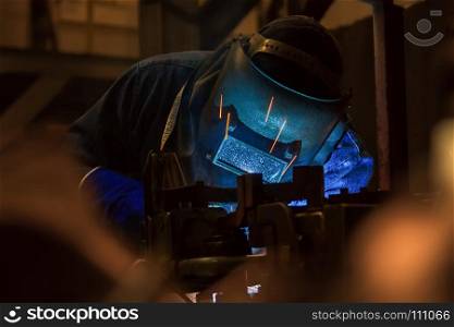 Industrial worker is welding metal part in factory