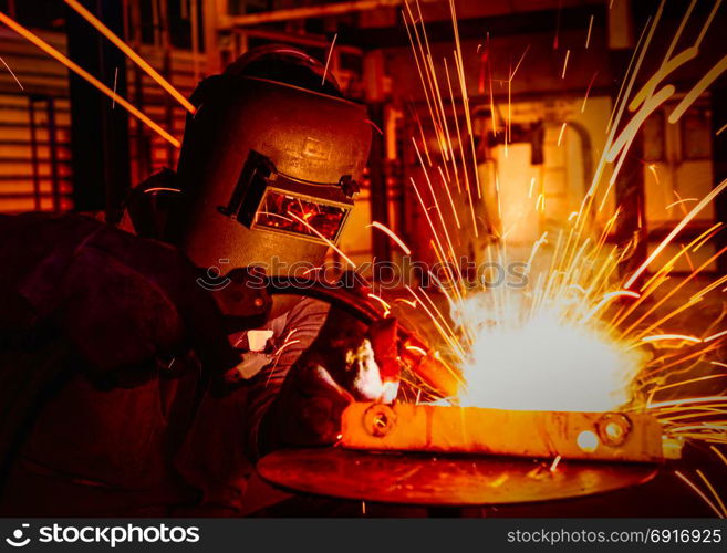 Industrial worker with protective mask is welding metal in car factory