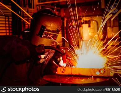 Industrial worker with protective mask is welding metal in car factory