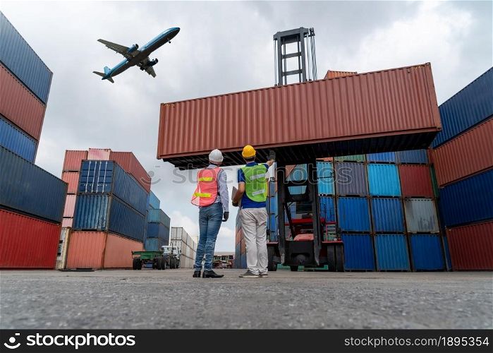 Industrial worker works with co-worker at overseas shipping container port . Logistics supply chain management and international goods export concept .. Industrial worker works with co-worker at overseas shipping container port