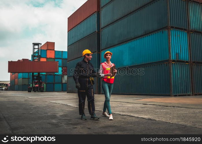 Industrial worker works with co-worker at overseas shipping container yard . Logistics supply chain management and international goods export concept .. Industrial worker works with co-worker at overseas shipping container yard