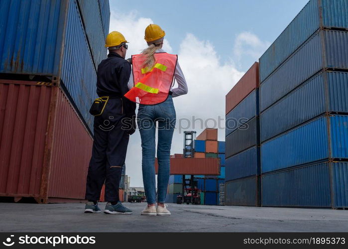 Industrial worker works with co-worker at overseas shipping container yard . Logistics supply chain management and international goods export concept .. Industrial worker works with co-worker at overseas shipping container yard