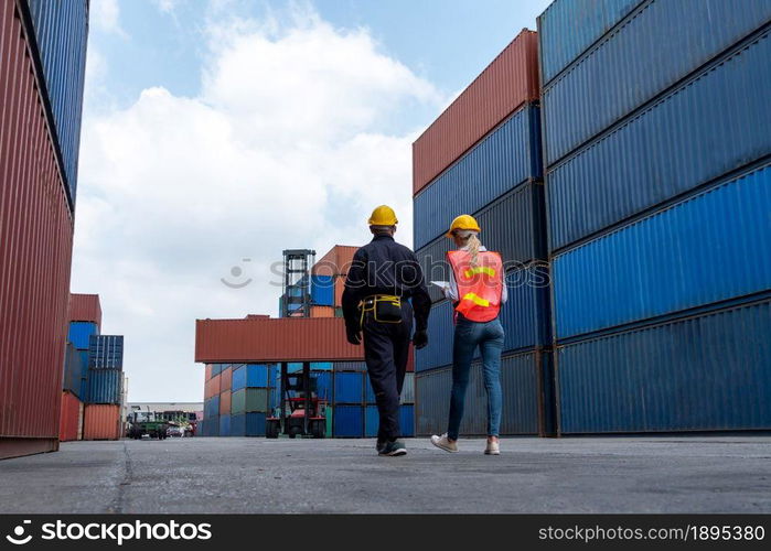 Industrial worker works with co-worker at overseas shipping container yard . Logistics supply chain management and international goods export concept .. Industrial worker works with co-worker at overseas shipping container yard