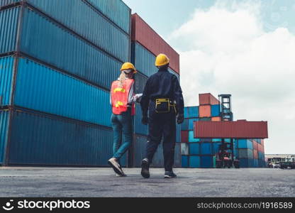 Industrial worker works with co-worker at overseas shipping container yard . Logistics supply chain management and international goods export concept .. Industrial worker works with co-worker at overseas shipping container yard