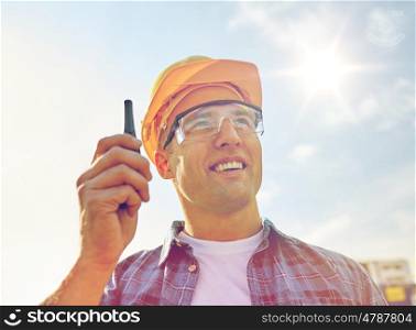 industry, building, technology and people concept - close up of male builder in hardhat with walkie talkie or radio outdoors