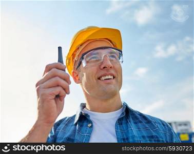 industry, building, technology and people concept - close up of male builder in hardhat with walkie talkie or radio outdoors