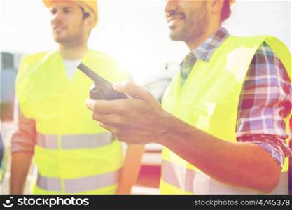 industry, building, technology and people concept - close up of male builders in high visible vests with walkie talkie or radio outdoors