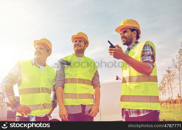 industry, building, technology and people concept - happy male builders in high visible vests with walkie talkie or radio outdoors