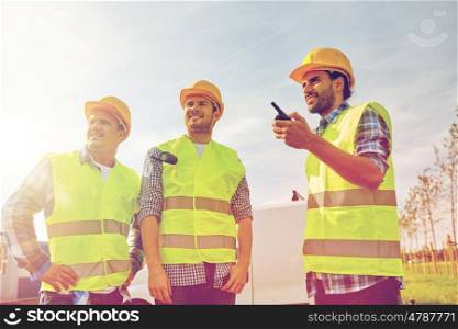 industry, building, technology and people concept - happy male builders in high visible vests with walkie talkie or radio outdoors