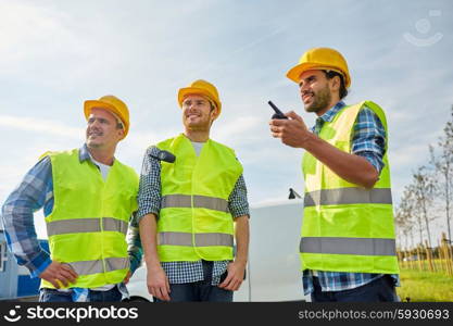 industry, building, technology and people concept - happy male builders in high visible vests with walkie talkie or radio outdoors