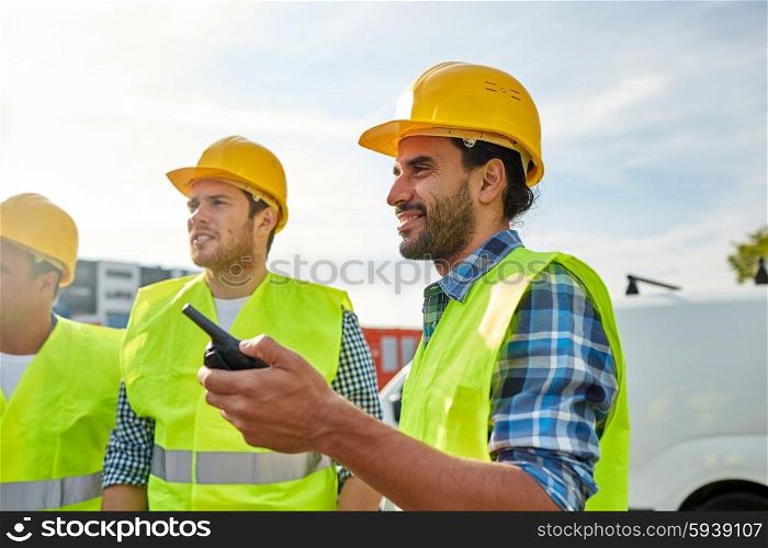 industry, building, technology and people concept - happy male builders in high visible vests with walkie talkie or radio outdoors
