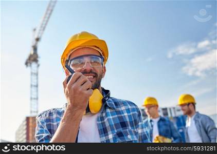 industry, building, technology and people concept -male builder in hardhat with walkie talkie or radio at construction site