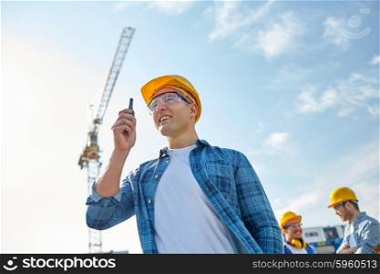 industry, building, technology and people concept -male builder in hardhat with walkie talkie or radio at construction site