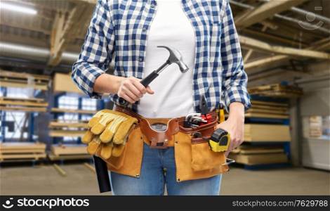 industry, production and job concept - close up of woman or worker with hammer and working tools on belt over factory workshop on background. female worker with hammer and tools on belt
