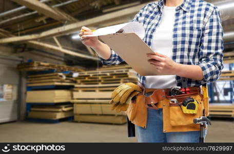 industry, production and job concept - close up of woman or worker with clipboard, pencil and working tools on belt over factory workshop on background. female worker with clipboard and working tools