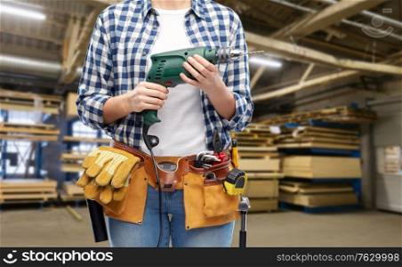industry, production and job concept - close up of woman or worker with working tools on belt with electric drill or perforator over factory workshop on background. woman or worker with drill and work tools