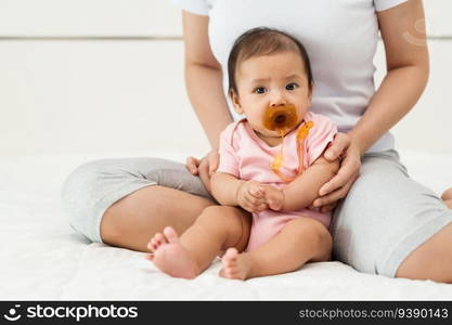 infant baby girl suck a pacifier with mother sitting on a bed