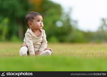 infant baby sitting on a green grass field at the park