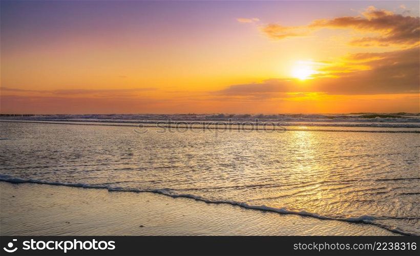 Infinite view of the sea with a cloudy sunset on a sandy beach on the Dutch coast of Zeeland