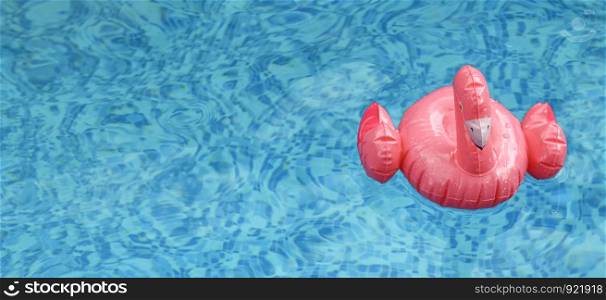 Inflatable pink flamingo float in transparent blue pool water. Top view on pink flamingo pool toy.