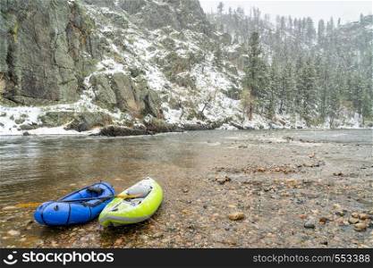 inflatable whitewater kayak and packraft on a shore of mountain river in heavy springtime snowstorm - Poudre River in northern Colorado