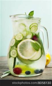 Infused water with cucumber, lemon, lime, berry and mint on blue background