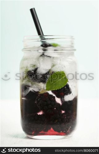 Infused water with fresh organic mulberry and mint on turquoise background