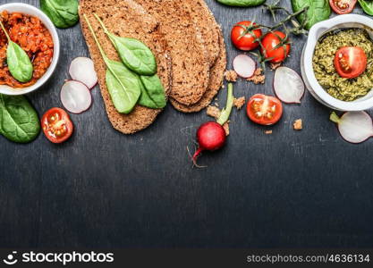 Ingredients and spread for vegetarian sandwich making on dark wooden background, top view, border