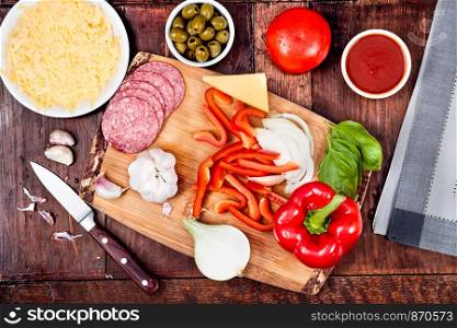 Ingredients, cheese, vegetables prepared for homemade pizza, on wooden board on the table. View from above