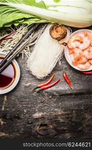 Ingredients for asian cooking: rice noodles, Bok choy (chinese cabbage) , soy sauce, shrimps, chili, and chopsticks on vintage rustic background, top view, place for text. Asian food concept.
