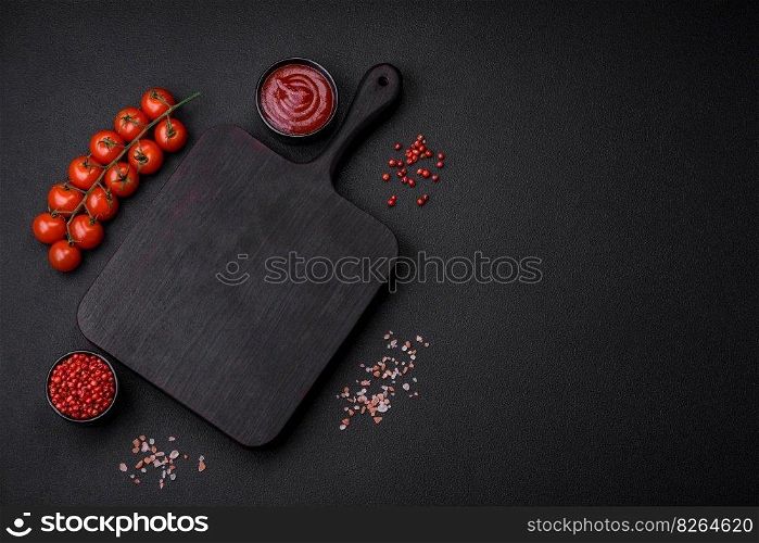 Ingredients for cooking cherry tomatoes, salt, spices and an empty cutting board on a dark concrete background