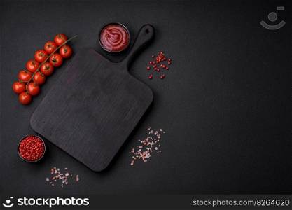 Ingredients for cooking cherry tomatoes, salt, spices and an empty cutting board on a dark concrete background