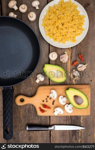 ingredients for cooking italian pasta - pasta, mushrooms, garlic, onions, avocado and frying pan