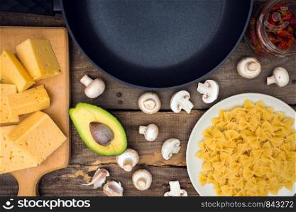 ingredients for cooking italian pasta - pasta, mushrooms, garlic, onions, avocado, cheese and frying pan
