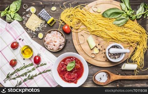 Ingredients for cooking pasta, tomatoes in own juice, basil, shrimp, grater, cherry tomatoes, wooden spoon, chopping board on wooden rustic background top view