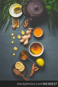 Ingredients for healthy turmeric spice tea on gray background with teapot, cup of tea,  lemon,  ginger, cinnamon sticks and honey , top view.  Immune boosting remedy , detox and dieting concept