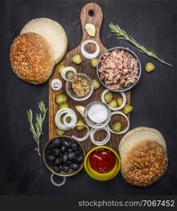 Ingredients for home kuking burger with tuna, pickled cucumbers, onions, olives and sauce on a cutting board on wooden rustic background top view close up