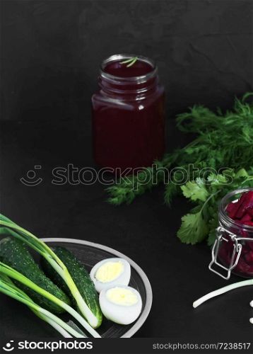 Ingredients for making cold borsch. Plate with boiled eggs and green herbs. In the background are cans with beetroot juice and pieces of beetroot. Black background. Close-up. Healthy, natural food.. Ingredients for making cold borsch. Plate with boiled eggs and green herbs. In the background are cans with beetroot juice and pieces of beetroot. Black background. Close-up.