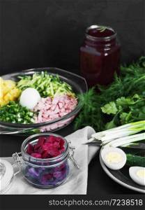 Ingredients for making cold borsch. Plate with boiled eggs and green herbs. Jars with beetroot juice and beetroot slices. Black background. Close-up.