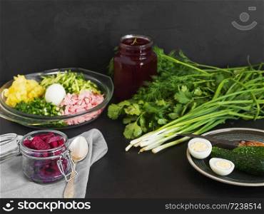 Ingredients for making cold borsch. Plate with boiled eggs and green herbs. Summer cold soup. Jars with beetroot juice and beetroot slices. Black background. Close-up.