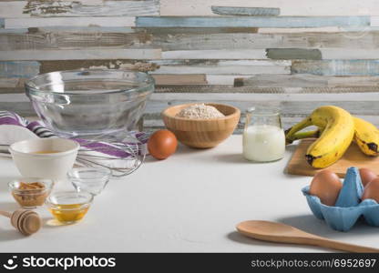 Ingredients for making pancake dough (eggs, oats flour, yogurt, banana, peanut butter, honey) on white wooden table.