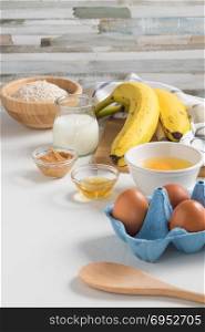Ingredients for making pancake dough (eggs, oats flour, yogurt, banana, peanut butter, honey) on white wooden table.