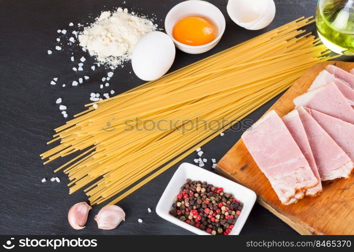 Ingredients for Pasta Carbonara on dark slate background. Spaghetti, ham, egg yolk, parmesan cheese, garlic and spices. Traditional italian cuisine. Top view, flat lay. Ingredients for Pasta Carbonara on black slate background