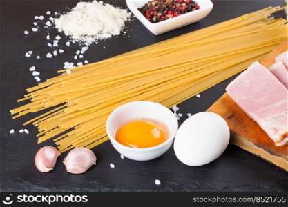 Ingredients for Pasta Carbonara on dark slate background. Spaghetti, ham, egg yolk, parmesan cheese, garlic and spices. Traditional italian cuisine. Ingredients for Pasta Carbonara on black slate background